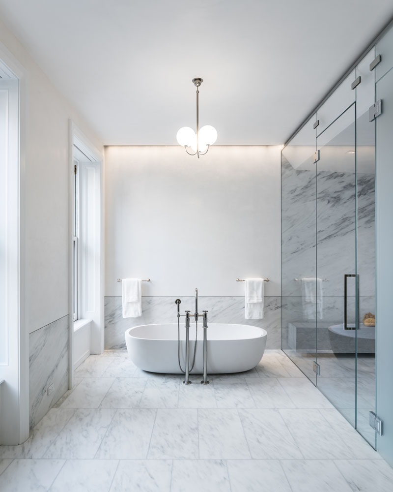 In this modern bathroom, a soaking tub by Boffi is outfitted with Waterworks taps, while a pendant light by Michael Anastassiades, hangs above it. #Bathroom #ModernBathroom #BathroomDesign