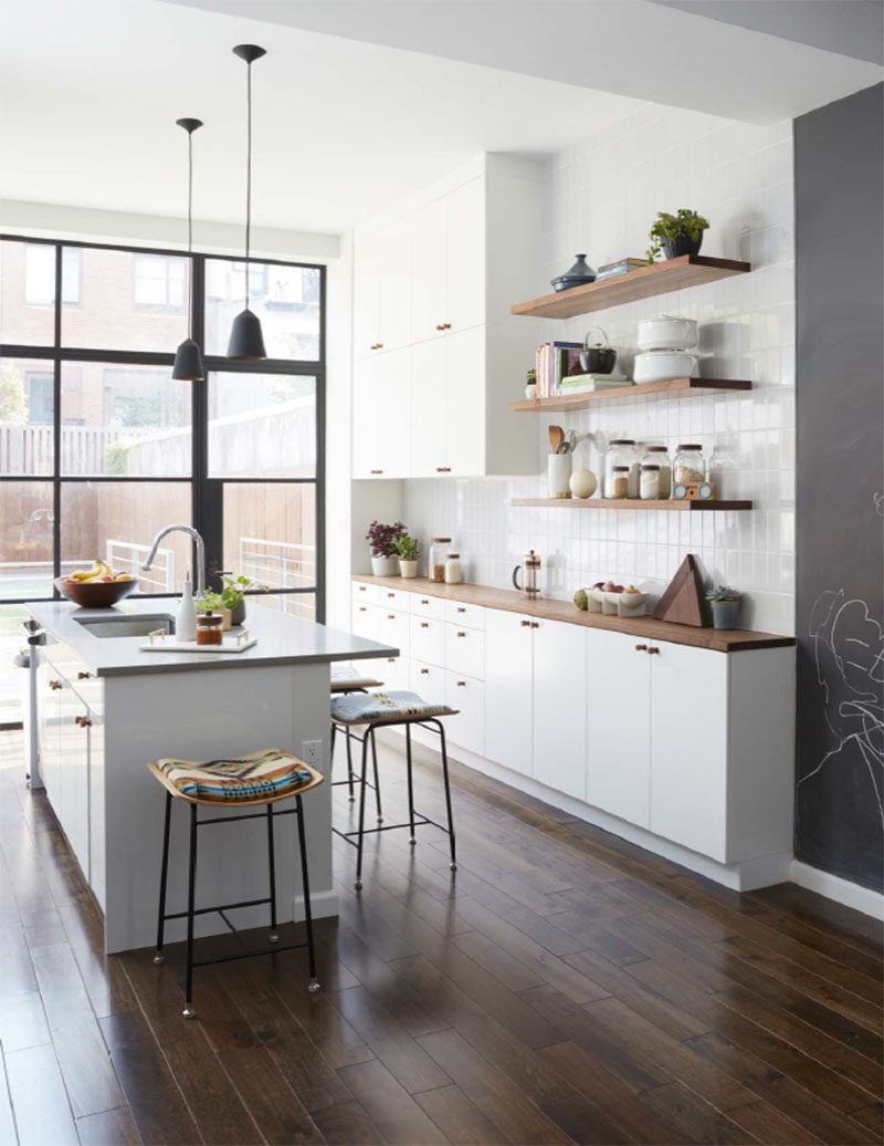 In this modern kitchen, white subway tiles laid vertically, and floating wood shelves complement the white cabinets and wood counters. #ModernKitchen #WhiteKitchen #WoodShelves