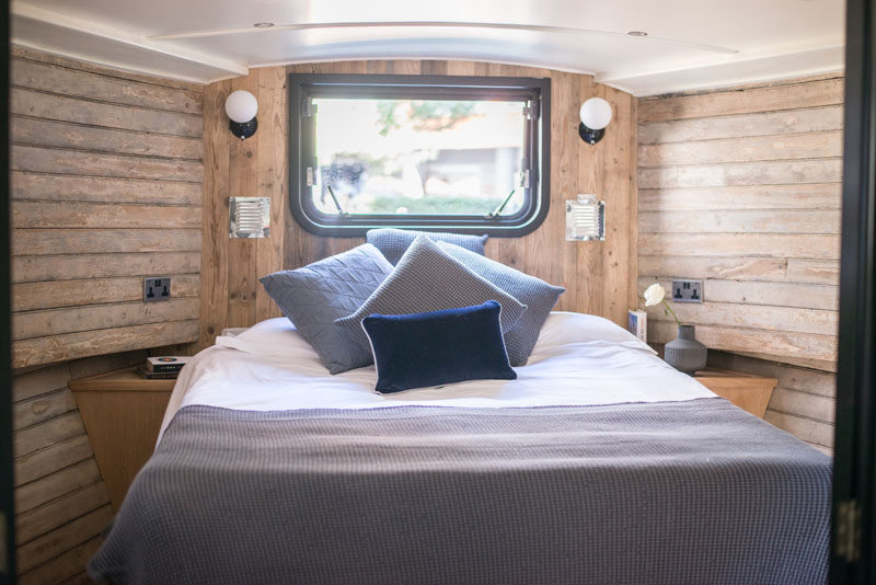 In the bedroom of a modern boathouse in London, built-in tables are positioned either side of the bed, while a window makes the room feel open. #Bedroom #ReclaimedWood #Boathouse