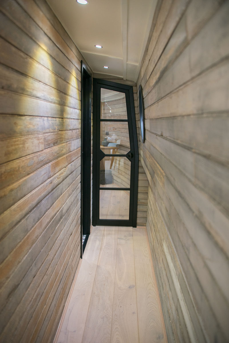 In this modern boathouse, a narrow wood-lined hallway leads to the bedroom and bathroom. #ReclaimedWood #WoodHallway #BlackFramedDoor