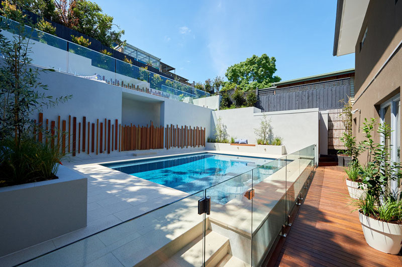 This modern backyard has a swimming pool, planter boxes with built-in seating, and an upper level with a curved lounge and grassy area. #Landscaping #ModernPool #PoolDesign #LandscapeDesign