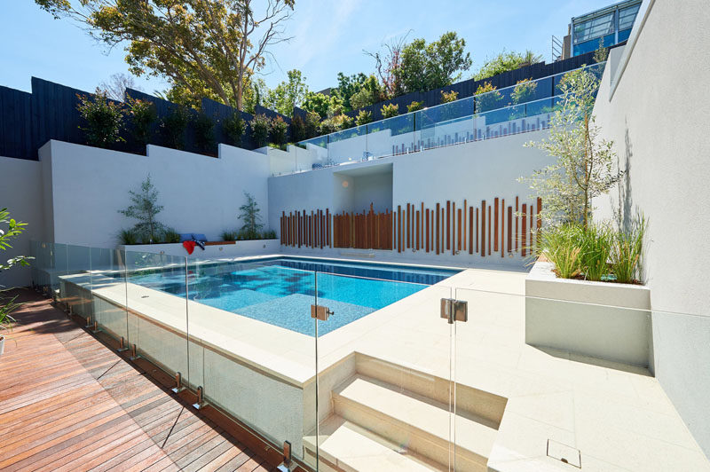 This modern backyard has a swimming pool, planter boxes with built-in seating, and an upper level with a curved lounge and grassy area. #Landscaping #ModernPool #PoolDesign #LandscapeDesign