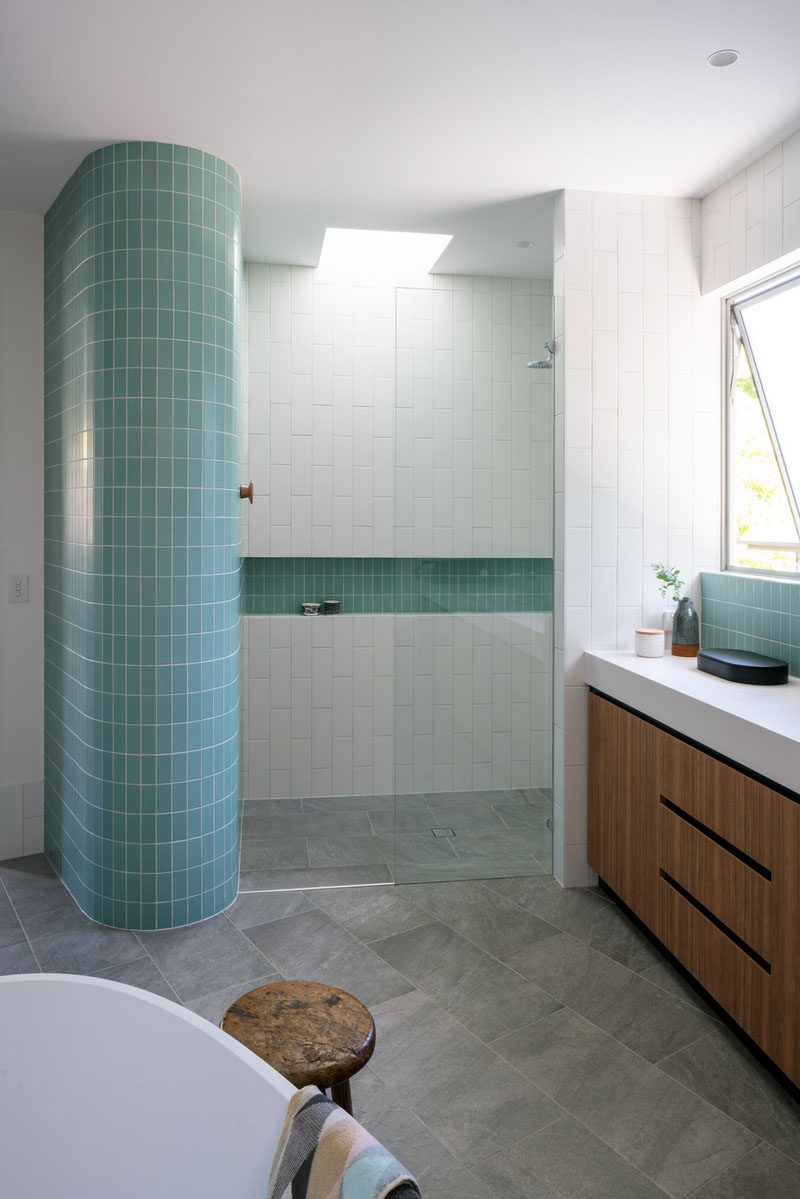 This modern bathroom features turquoise tiles that wrap around a curved wall, while white subway tiles have been laid vertically, drawing your eye upwards to the small skylight in the shower. #ModernBathroom #Tiles #Skylight #Shower