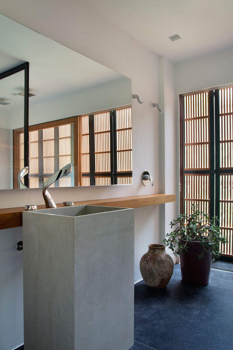 In this modern bathroom, a large mirror reflects the natural that comes through the wooden slat, while a sliding wood framed glass door can be opened to have a breeze flow through the room. #BathroomDesign #ModernBathroom