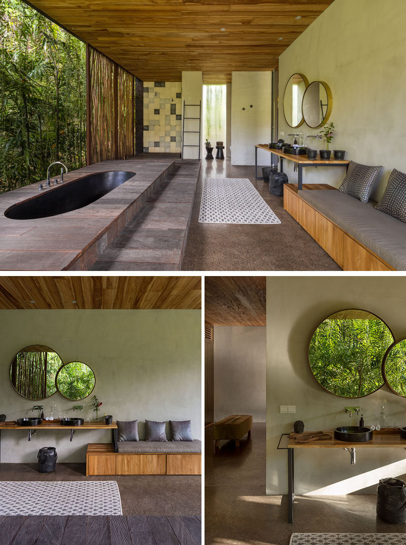 In this modern bathroom, a black sunken bathtub is positioned for relaxing tropical garden views.