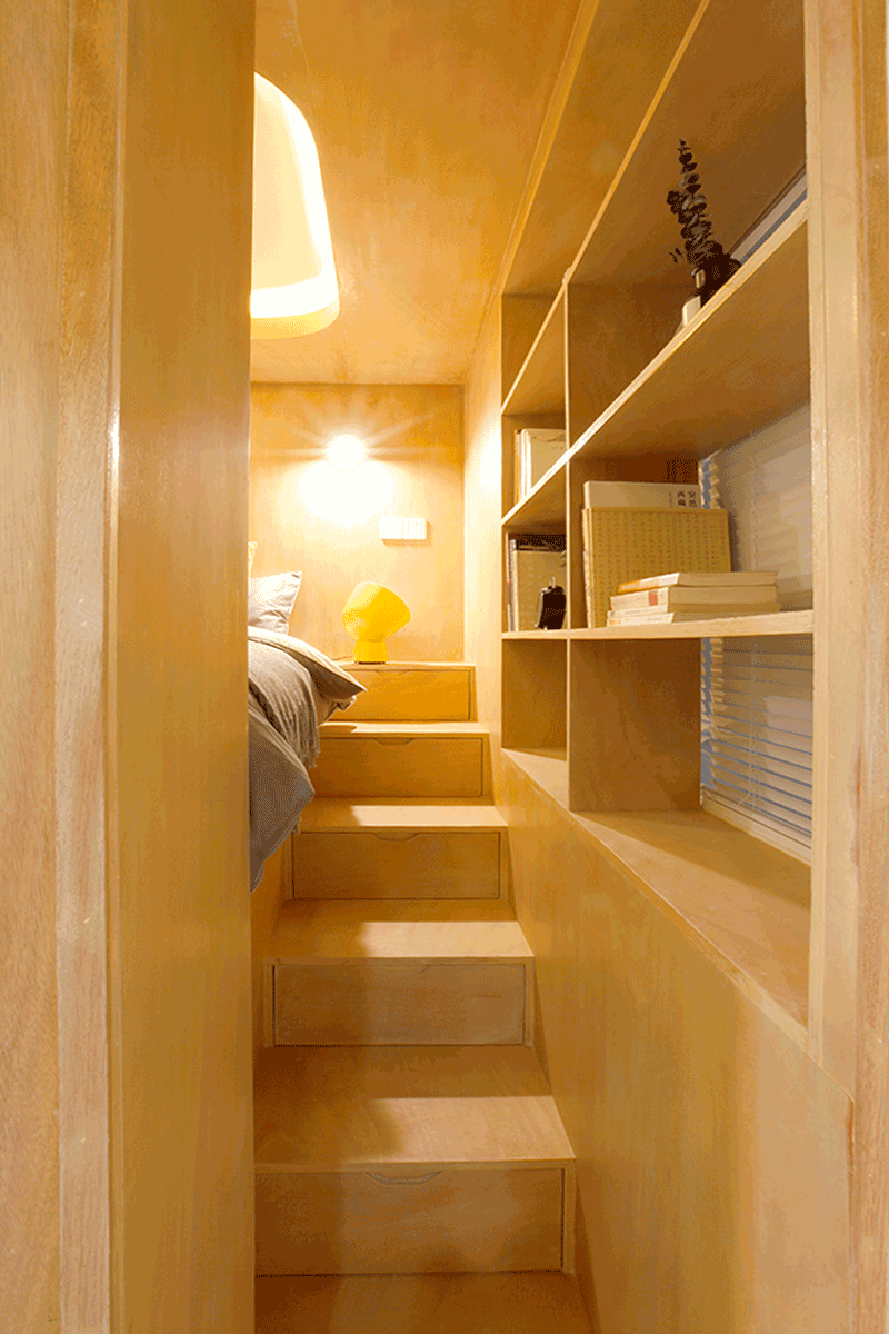 This small apartment makes use of the ceiling height to raise the bed up and place it within a wood box, and therefore allowing storage to be included under the bed and within the stairs. #Bedroom #RaisedBed #PlatformBed #BedroomDesign #ModernBedroom #Stairs #Storage