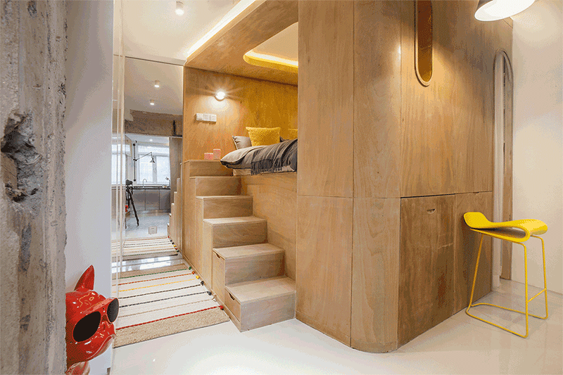 This small apartment makes use of the ceiling height to raise the bed up and place it within a wood box, and therefore allowing storage to be included under the bed and within the stairs. #Bedroom #RaisedBed #PlatformBed #BedroomDesign #Stairs #StairsWithStorage