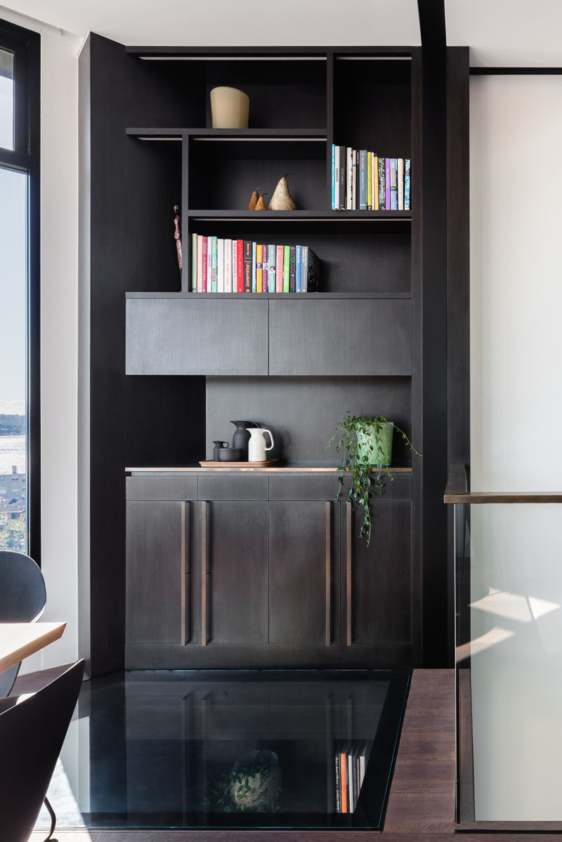 This modern home features a custom designed dark wood shelving unit, and on the floor is a glass section that lets light travel through to the level below. #GlassFloor #Shelving