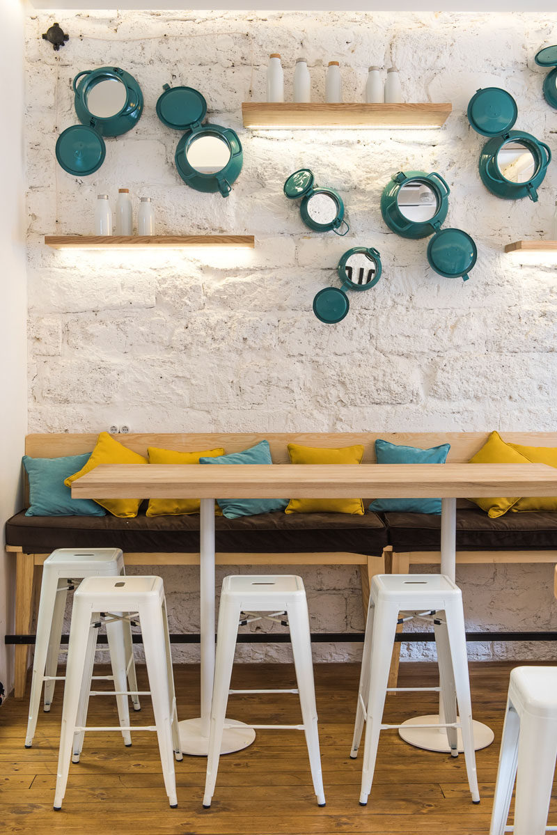 This modern cafe features a textured wall that's been decorated with painted portholes, floating wood shelves, and a long communal table with stools and seating. #ModernCafe #CafeDesign #Shelving #WallDecor