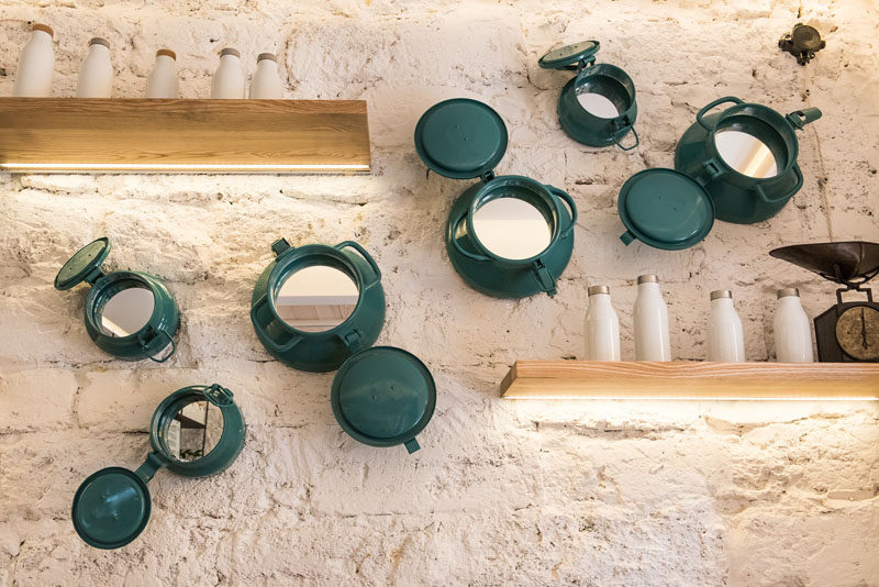 This white textured wall features blue accents in the form of portholes that have mirrors inside them, reflecting the rest of the modern cafe interior. #FloatingShelves #WallDecor #Portholes