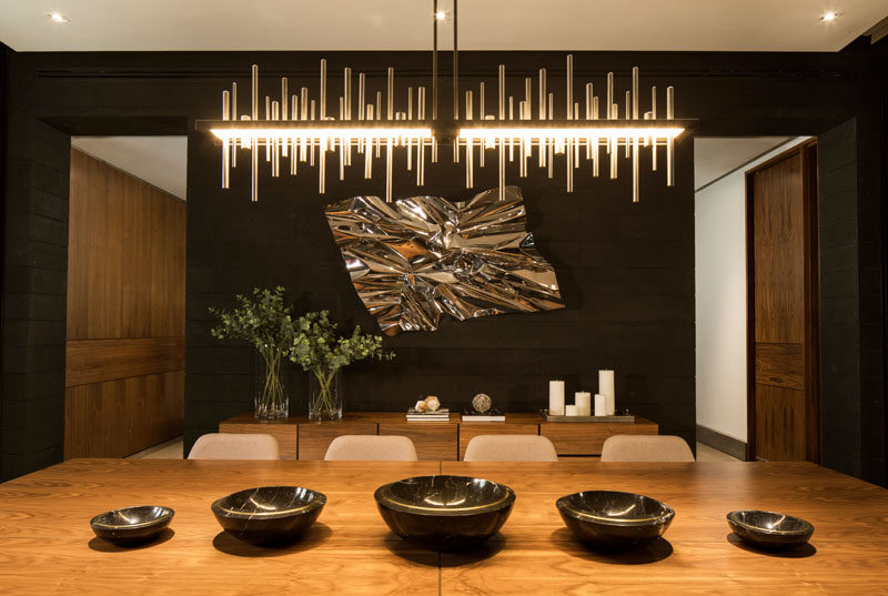 In this modern dining room, a sculptural chandelier brightens the room, while the light is reflected in the metallic wall sculpture. #DiningRoom #ModernDiningRoom #InteriorDesign