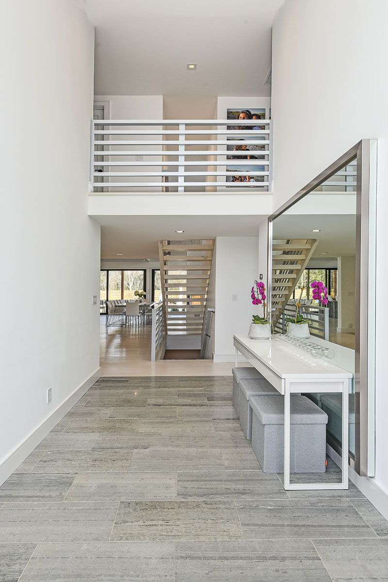 Stepping inside this modern house, the entryway has a high ceiling with tiled flooring and a view of the stairs and upper level. #Entryway #ModernEntryway #InteriorDesign