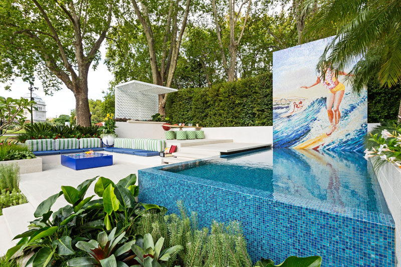 Inspired by the Hawaiian word Ohana, meaning ‘Family’, this modern garden sets out to portray a relaxing family space, specifically geared to the family with teenage kids. It has a pool with a large mural, a dining area with outdoor kitchen, and a lounge area with a firetable. #Landscaping #GardenDesign #Pool #OutdoorDining #LandscapeDesign