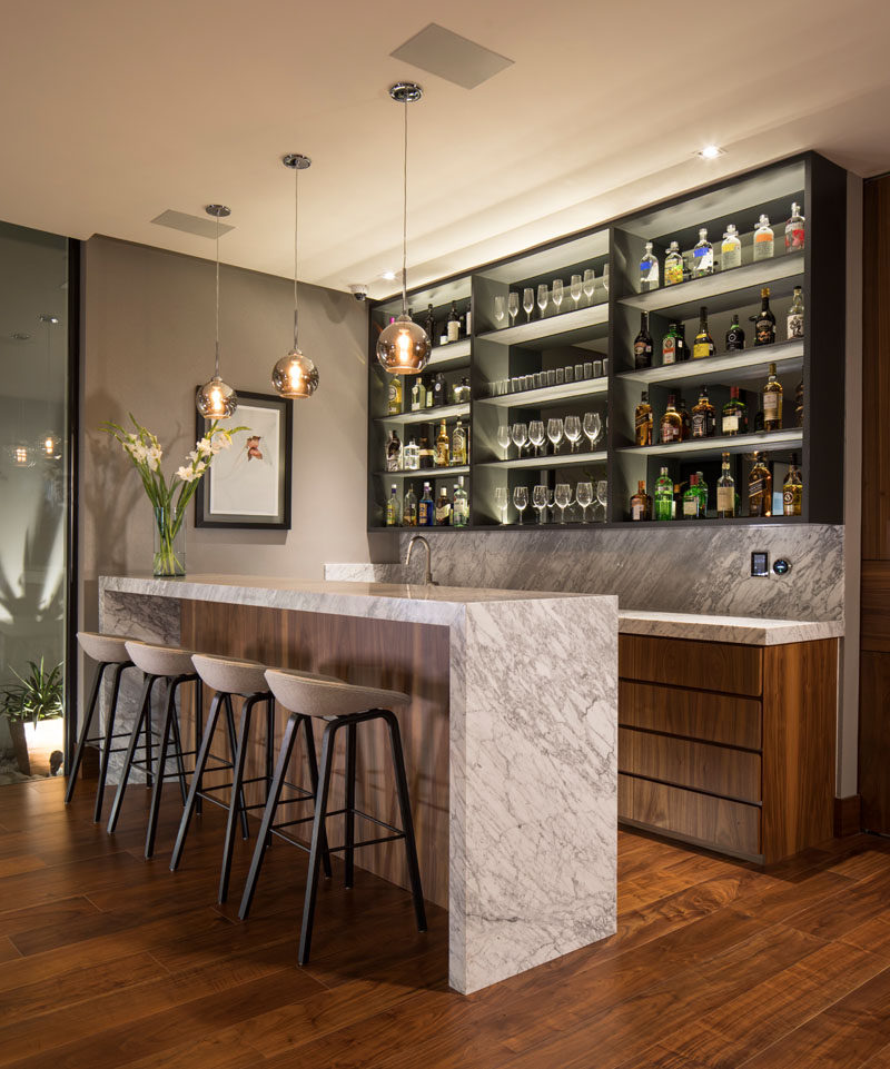 This modern house has a bar that features a shallow shelf with a mirrored back and hidden lighting to highlight the bottles and glassware. #Bar #HomeBar #InteriorDesign