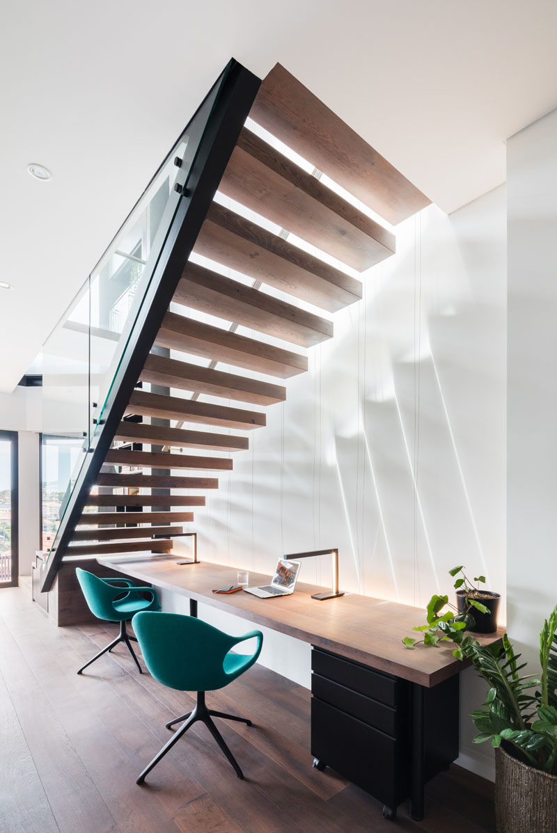 Cantilevering stairs with wood treads and a steel balustrade lead down to the lower level of this modern house. Underneath the stairs is desk with a wood work surface that's large enough for two people. #ModernStairs #CantileveredStairs #HomeOffice