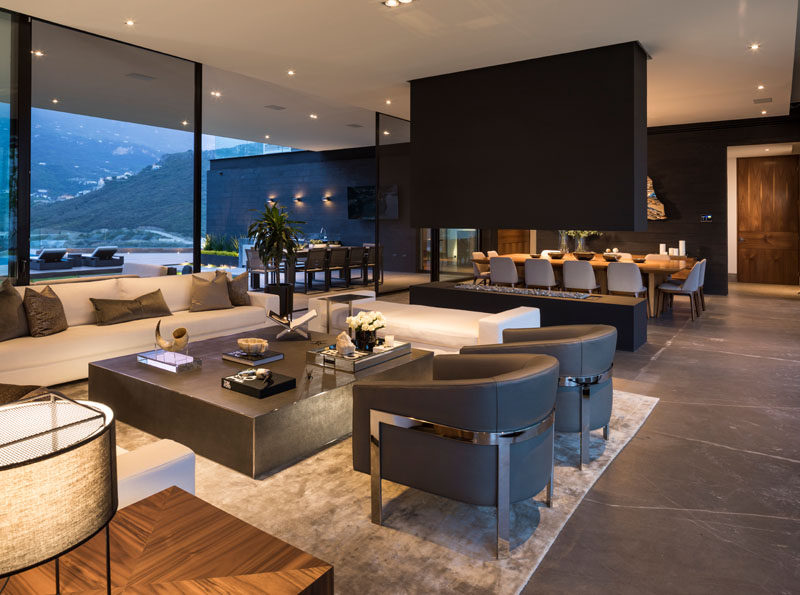 Large sliding glass doors open to connect the exterior and interiors spaces of this modern house, with the living room separated from the dining room by an open fireplace. #Fireplace #LivingRoom #InteriorDesign