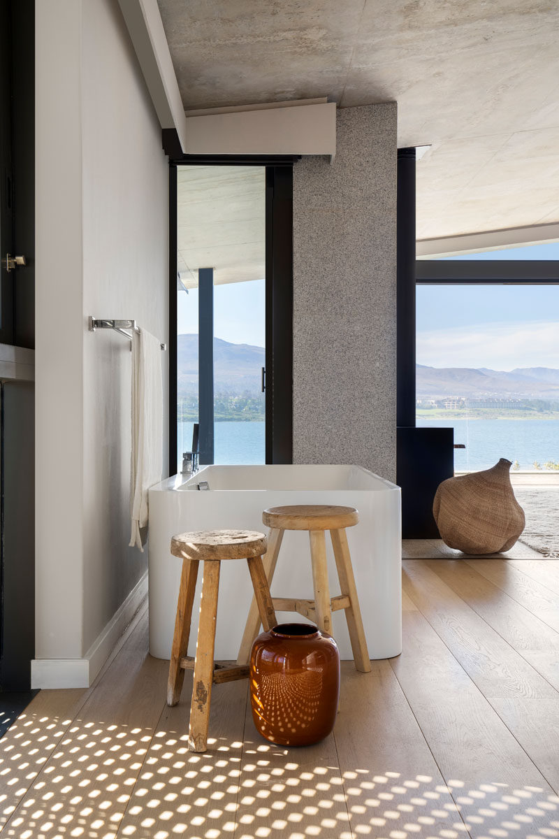 In this modern bathroom that's open to the bedroom, wood flooring adds warms to the space, while a vertical window provides a glimpse of the view from the bathtub. #ModernBathroom #FreestandingBathtub