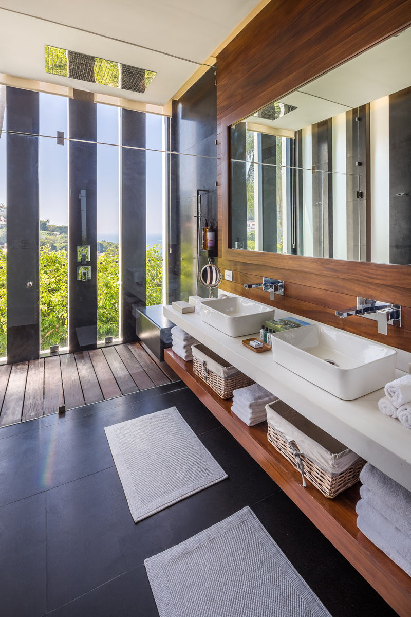 In this modern bathroom, floor to ceiling glass separates the shower from the vanity, while narrow vertical windows give a glimpse of the tree view outside. #MasterBathroom #DualVanity #BathroomDesign #ModernBathroom