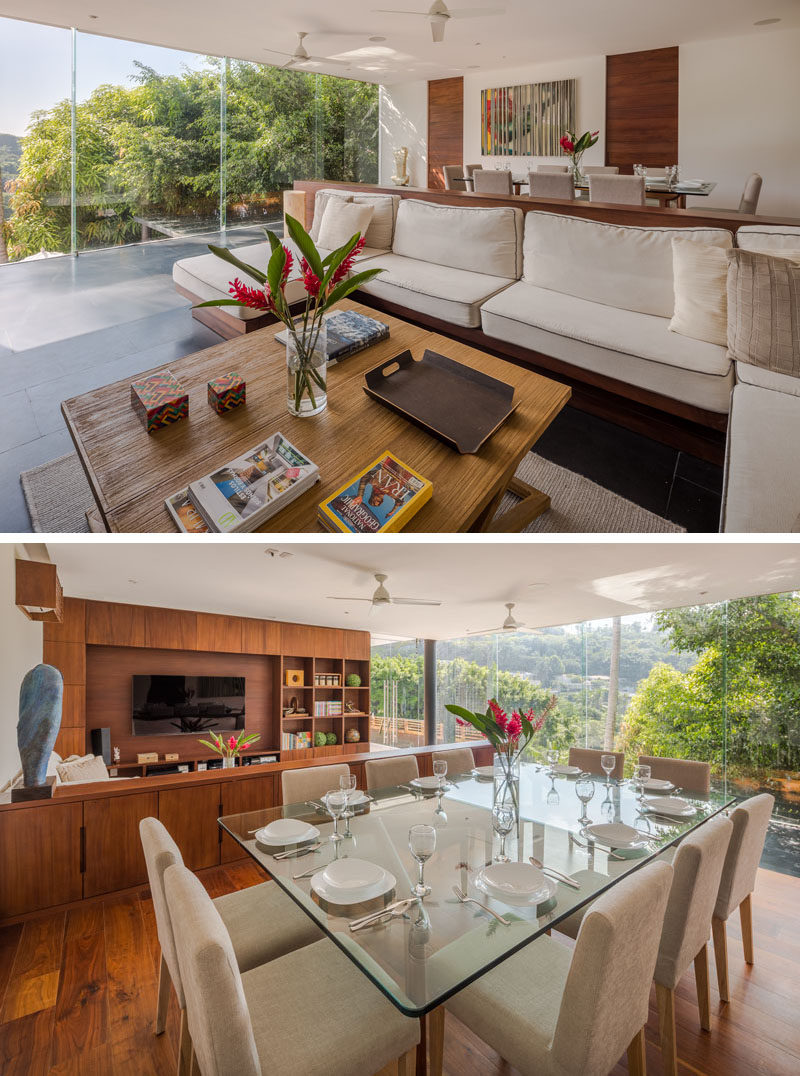 In this modern house, there's an open plan dining and living room, with the living room featuring a couch with wood cabinetry behind it. #LivingRoom #DiningRoom #Windows