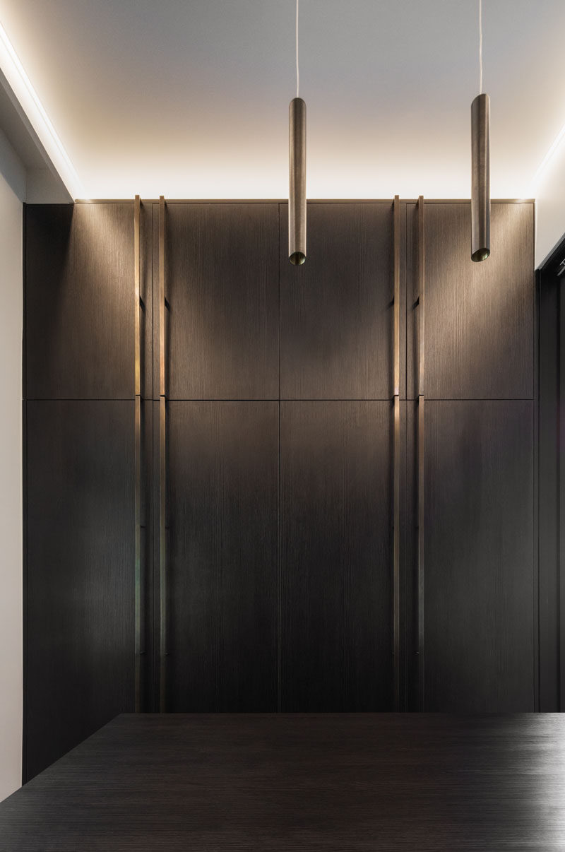 In this modern walk-in closet, dark cabinetry has been combined with bronze hardware. #DarkCabinetry #BronzeHardware #WalkInCloset