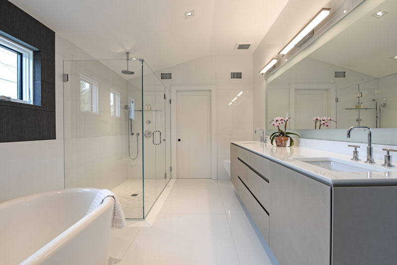 This modern bathroom features a grey vanity and white freestanding bathtub. A glass shower surround helps to keep the bathroom feeling bright and open. #ModernBathroom #GreyVanity #GreyAndWhite