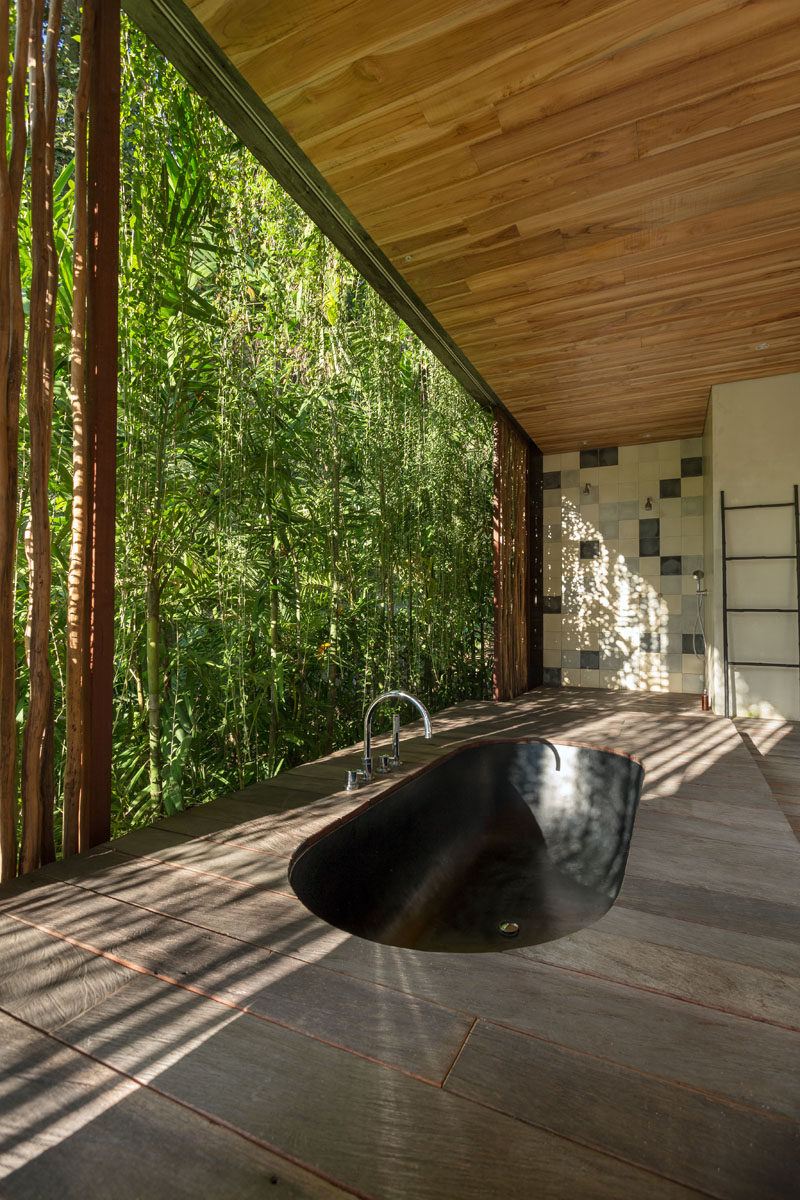 In this modern bathroom, a black sunken bathtub surrounded by wood is positioned for relaxing tropical garden views. #SunkenBathtub #BlackBathtub #TropicalBathroom #ModernBathroom