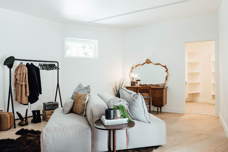 This contemporary dressing room is furnished with a couch, vanity, and freestanding clothes rack. The dressing room also has access to a walk-in closet filled with shelves. #DressingRoom #InteriorDesign