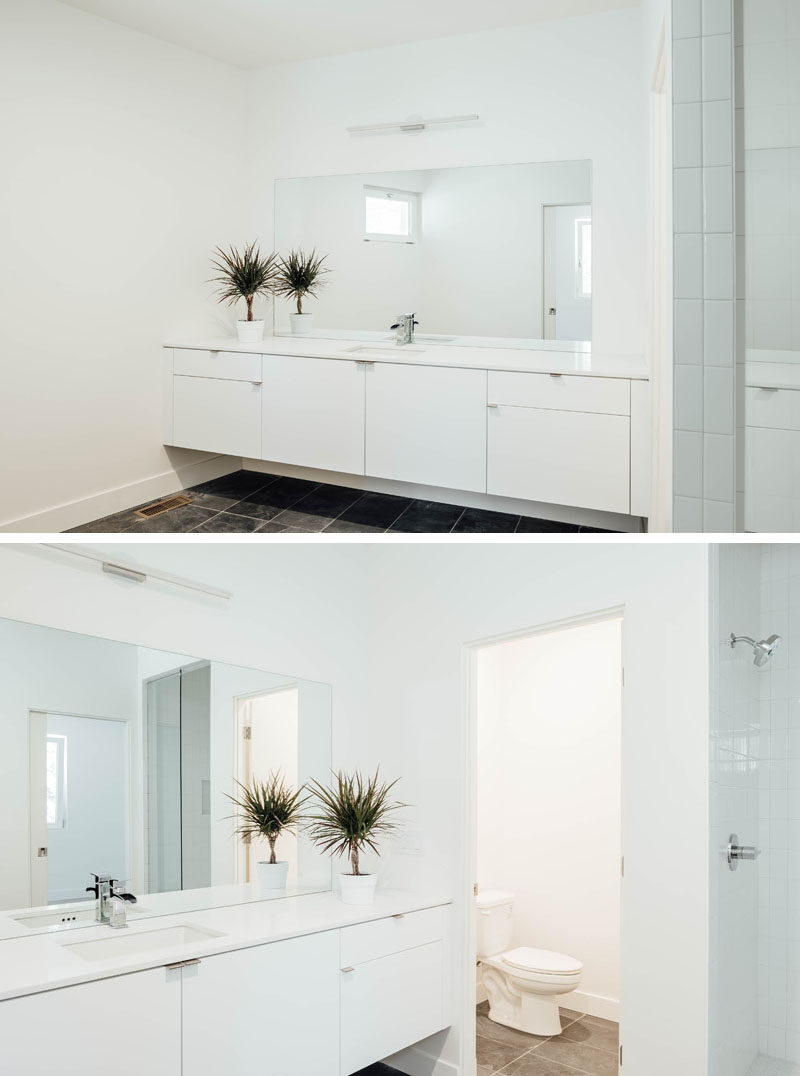 In this white bathroom, a floating vanity runs the length of the wall, and a large mirror reflects light throughout the space. #ModernBathroom #WhiteBathroom #BathroomDesign