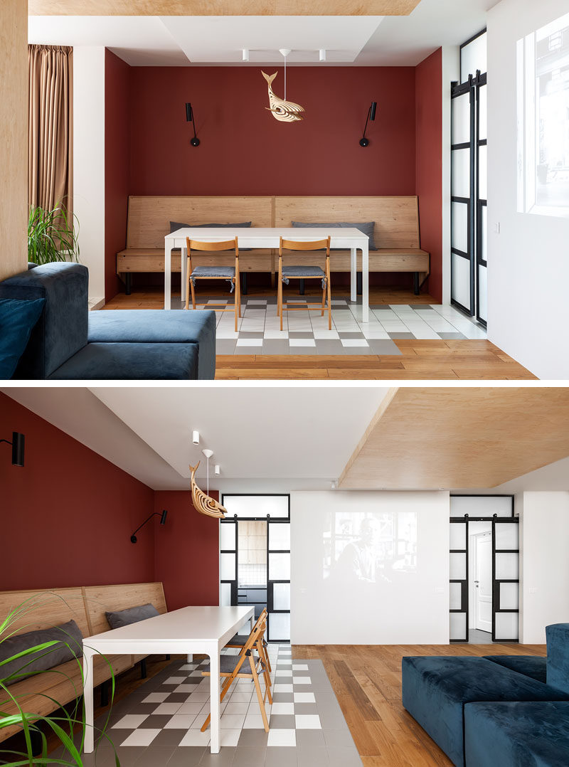 Tucked into an alcove in this modern apartment is the dining area, that's defined by deep red walls and custom  design wood banquette seating. Grey and white tiles lead to the kitchen. #DiningAlcove #BanquetteSeating #DiningRoom