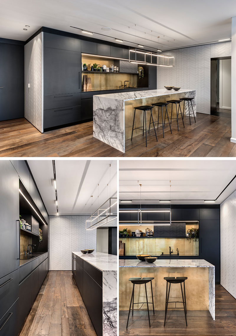 In this modern kitchen, matte black cabinets have been combined with a gold metallic backsplash and an island with a marble countertop that wraps down the sides to meet the floor. #ModernKitchen #KitchenDesign