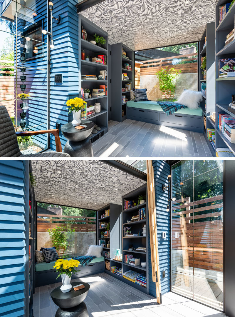 Underneath the loft bed in this modern backyard studio is an additional seating area with a built-in day bed next to a large window. The decorative wallpapered ceiling hides speakers designed to be hidden behind drywall, that are mounted in the ceiling, under the loft. #BackyardStudio #BackyardRetreat #DayBed #BuiltInBench #Bookshelves