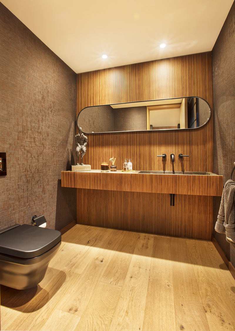 In this modern powder room, a wood accent wall is the backdrop for the vanity and long horizontal mirror. #PowderRoom #ModernBathroom