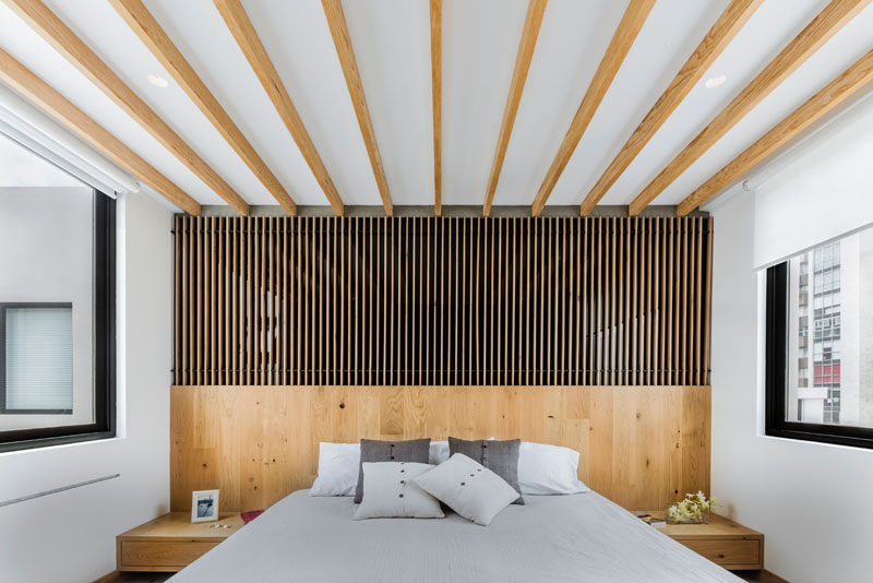 In this modern master bedroom, wood accents add warmth to the white room, while the windows on both sides allow plenty of natural light to fill the room. #Masterbedroom #BedroomDesign #WoodAccentWall