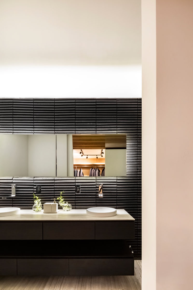 In this modern master bathroom, a black accent wall strongly contrasts the white ceiling, while a blacklit mirror helps to highlight the wall detail and the vanity. #ModernBathroom #BlackBathroom #BacklitMirror