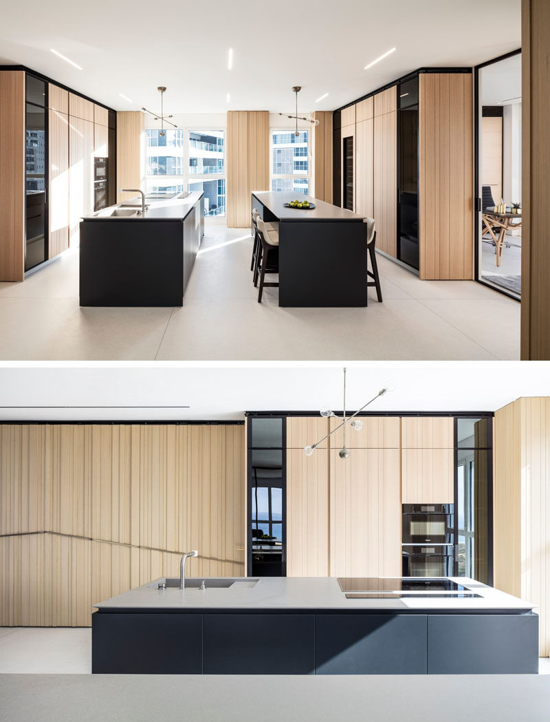 This modern kitchen uses the same wood on the cabinets that's featured on the walls. Two black islands with white countertops create a contrast to the light wood. #ModernKitchen #WoodKitchen #BlackKitchenIsland #KitchenDesign