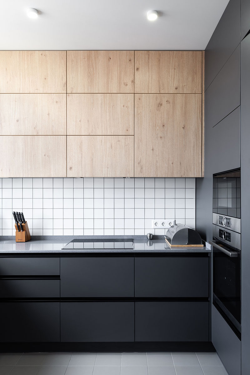 In this modern kitchen, black cabinetry contrasts the white tiles, while upper wood cabinets add a natural touch. #ModernKitchen #BlackCabinets #KitchenDesign