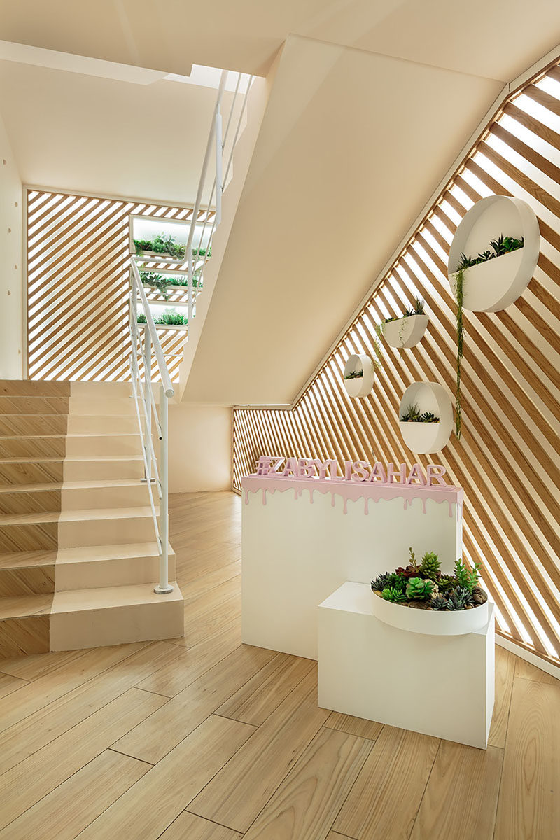 Upon arrival at this modern cafe, stairs with walls of back-lit diagonal wood slats and planters lead upstairs. #Stairs #AccentWall #InteriorDesign