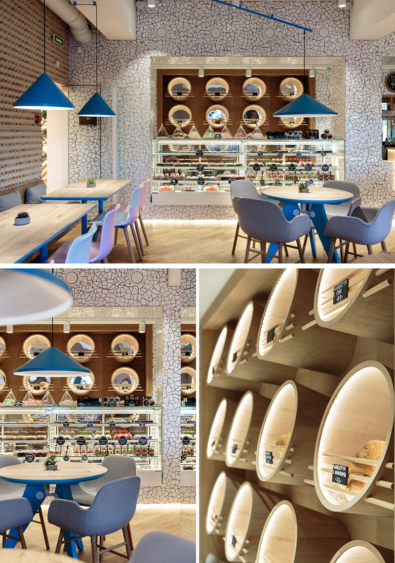 In this modern cafe, chipped white tiles have been installed on the wall surrounding the service area, and deep custom wood circles with mirrors and hidden lighting hold the various items for sale. #Cafe #CafeDesign #InteriorDesign #RetailDesign