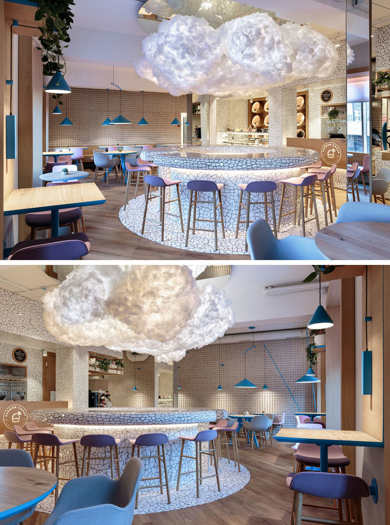 A large cloud light hangs in the middle of this modern cafe above a circular bar area, that features a white chipped tile surface. #Cafe #CafeDesign #InteriorDesign #CloudLight