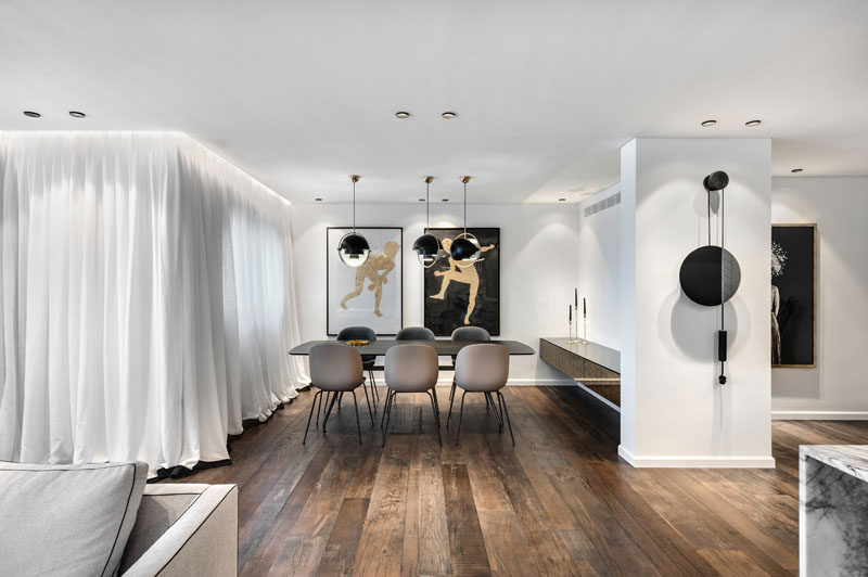 This modern apartment has a dining area anchored by three pendant lights, while a white curtain warps around the interior to provide privacy when needed. #DiningRoom #WoodFloors #Curtain