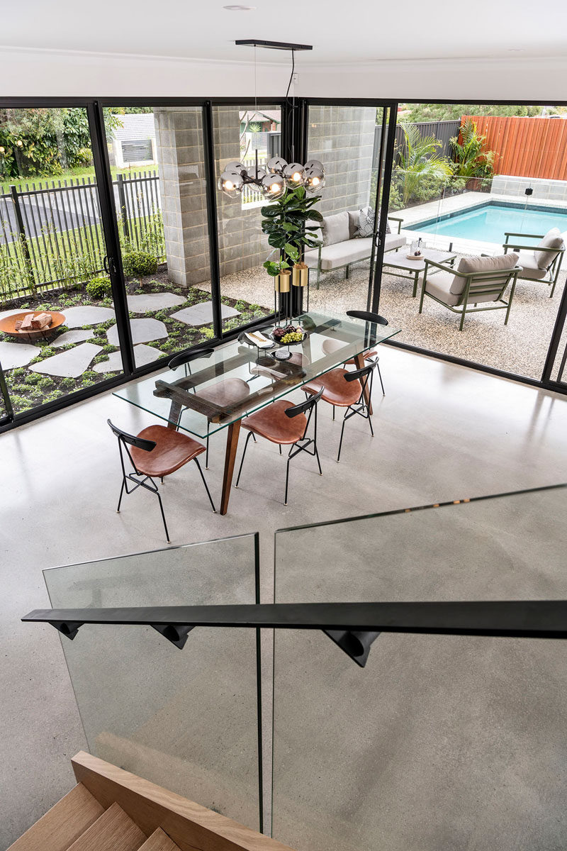 Walls of glass with sliding doors open to connect the interior and exterior living spaces of this modern house. The dining room features a glass dining table with a chandelier hanging above. #ModernHouse #ConcreteFloors #DiningRoom #OutdoorSpaces #GlassWalls