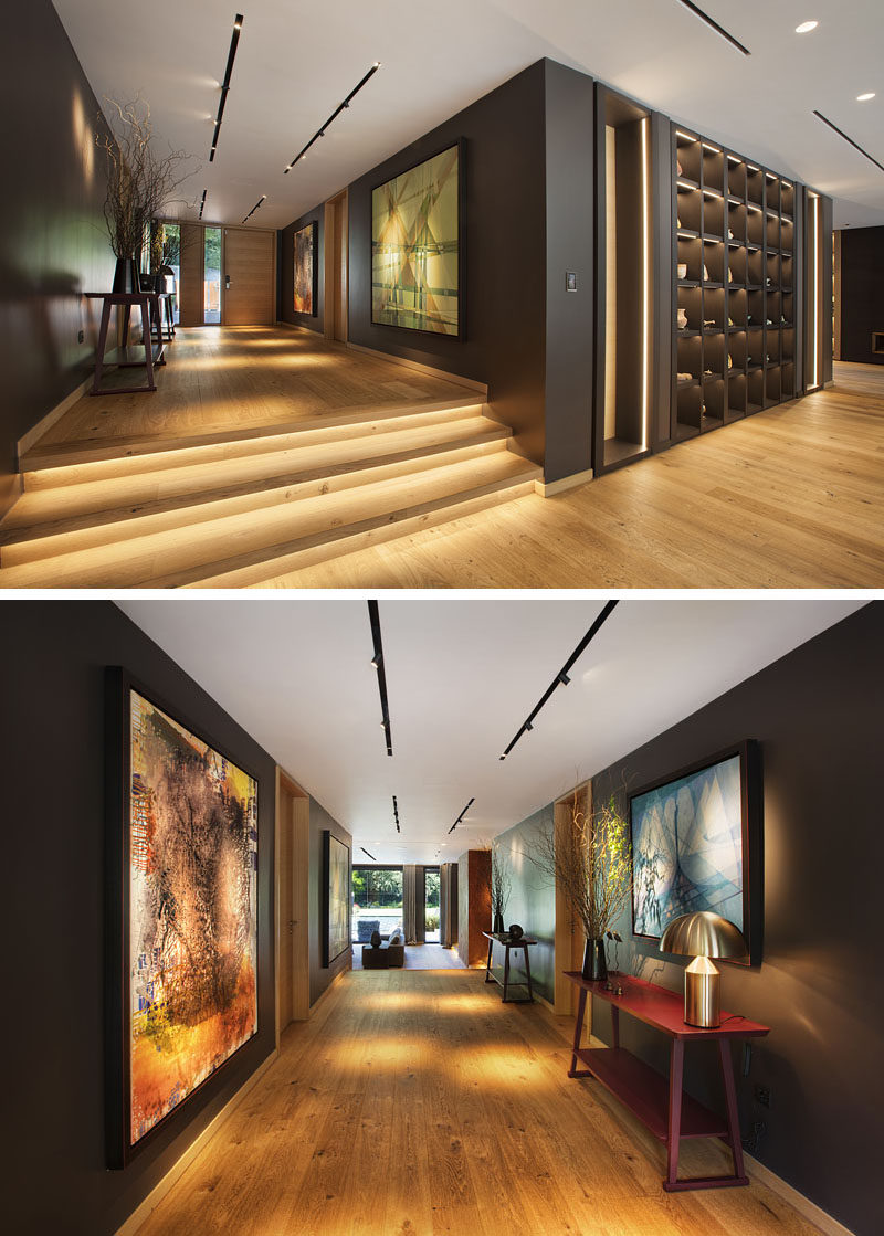 Inside this modern house, wood has been used to create a warm and inviting living space. In the entryway hallway, dark walls contrast the wood flooring, while track lighting highlights artwork. #Entryway #Hallway #Steps