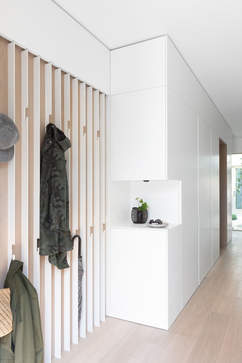 This modern entryway features a wall of bespoke slatted steel coat hook, and a small open shelf cut out in the white cabinetry. #ModernEntryway #InteriorDesign