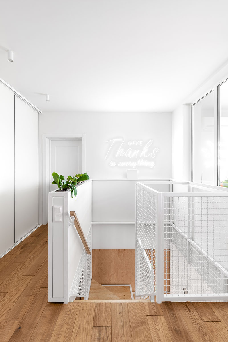 At the top of these modern wood stairs, there's a pony wall with built-in planters, and white walls help to reflect the light coming in from the window. #InteriorDesign #Planters