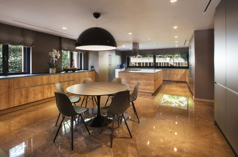 This modern kitchen makes use of marble and wood. A small dining area is centrally located under a black glossy dome pendant light. #ModernKitchen #KitchenDesign