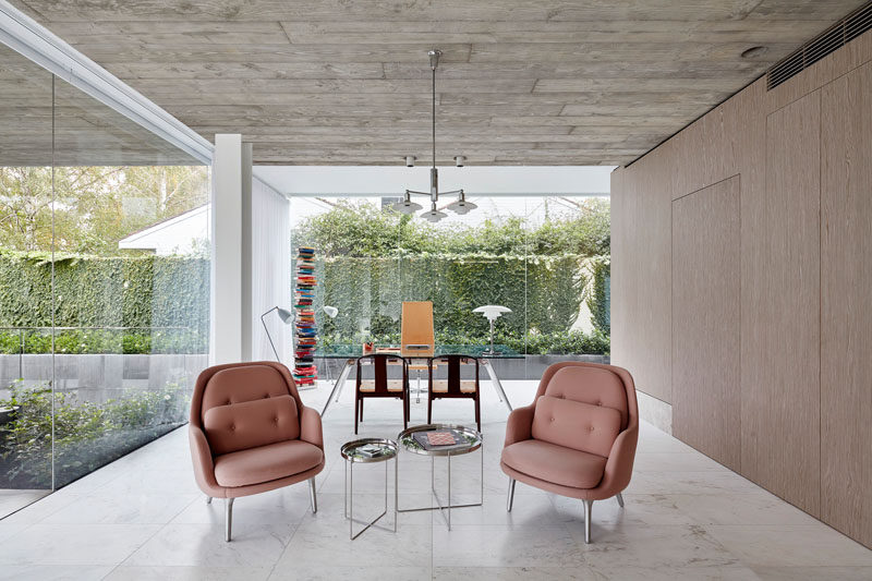 This modern house has a combined home office and sitting area. Walls of glass provide views of the front garden and ivy covered walls. #ModernHomeOffice #GlassWalls