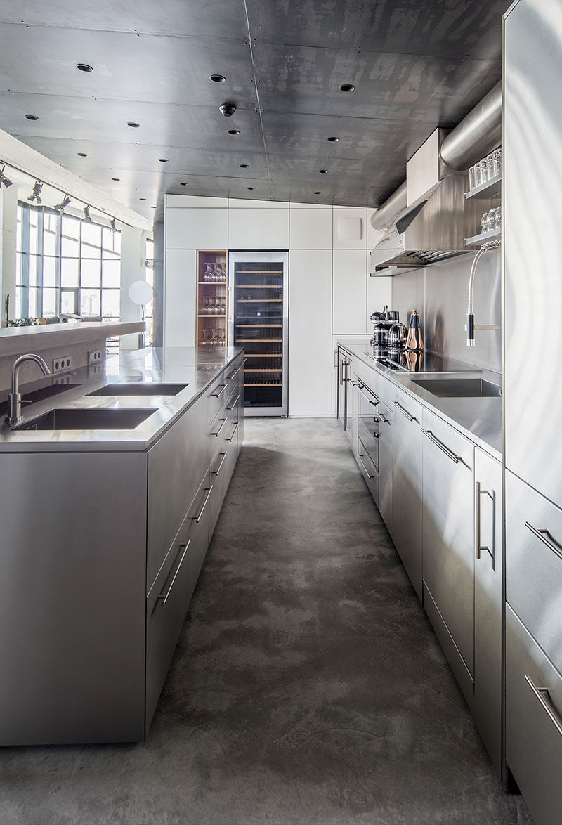 This modern kitchen features concrete flooring, a built-in wine fridge, and stainless steel cabinetry that complements the steel ceiling.