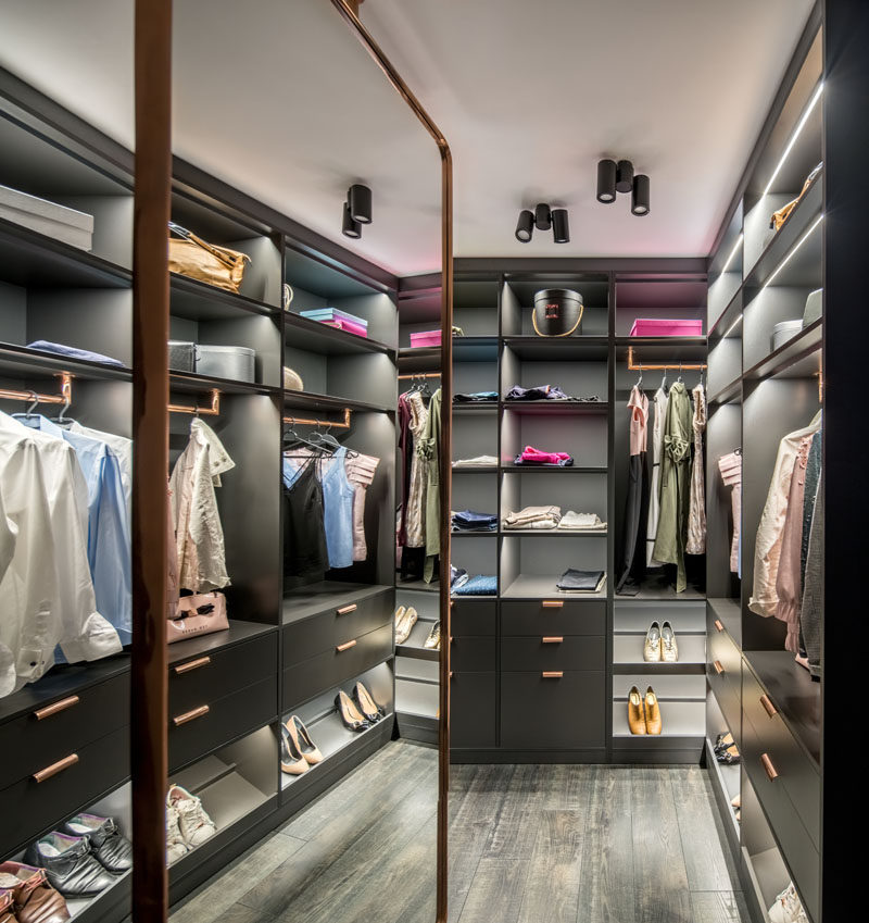 This modern walk-in closet has custom shelving with lighting that fills the walls, and a large mirror. #WalkInCloset #InteriorDesign #Storage