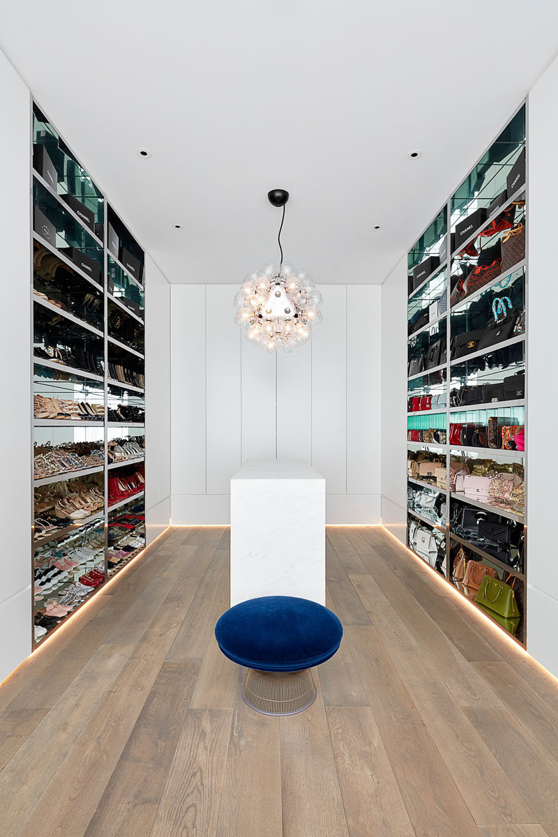 In this modern walk-in closet, the walls are lined with open shelves that have mirrored interiors, while a central island provides additional storage for accessories and smaller items. #WalkInCloset #DressingRoom #InteriorDesign