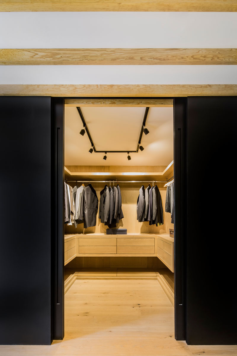 Hidden behind sliding black doors is a walk-in closet, that once opened, reveals a warm wood interior and plenty of storage for clothes. #WalkInCloset #InteriorDesign